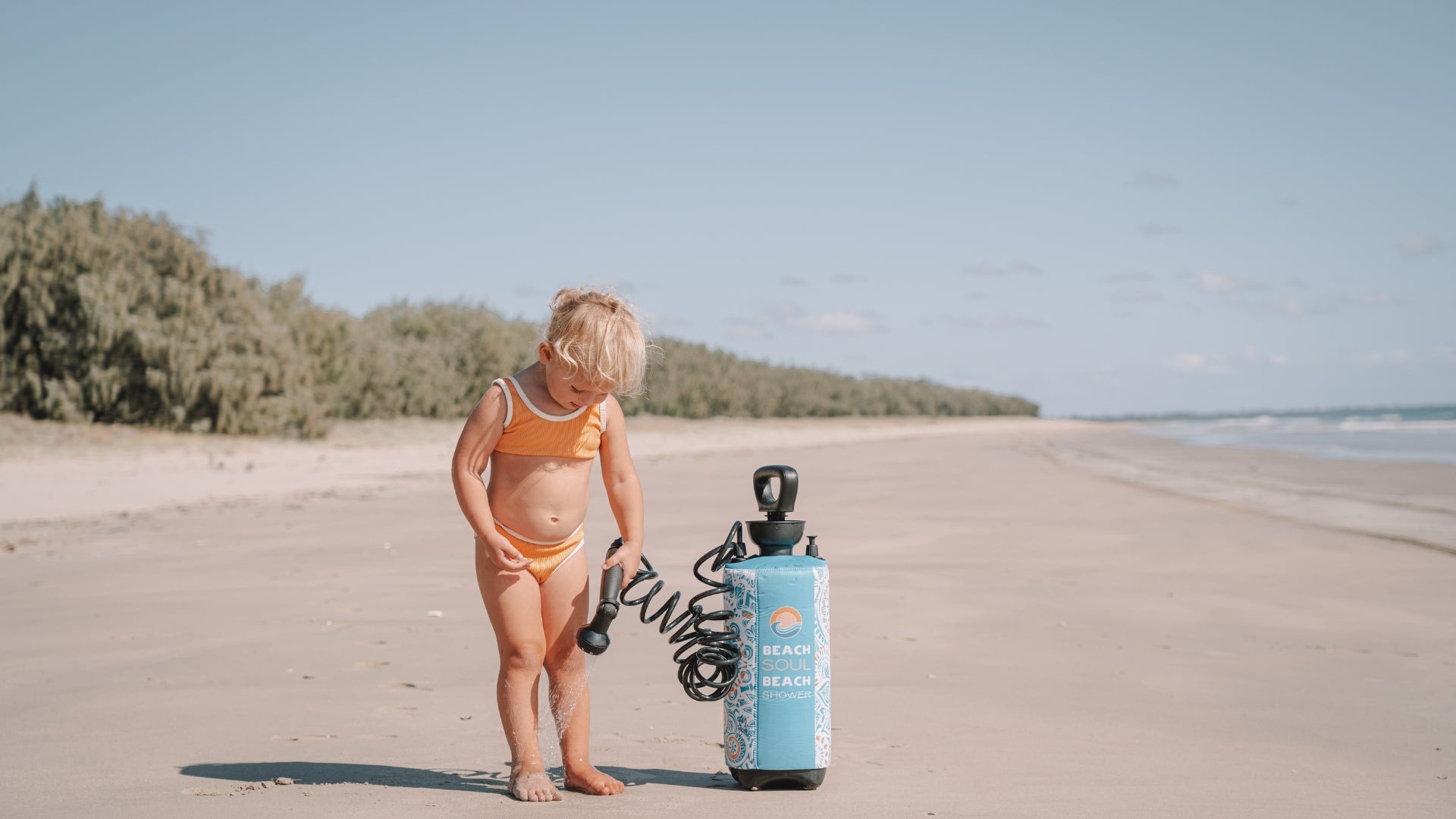 Child standing beside a Beach Soul portable shower at the beach