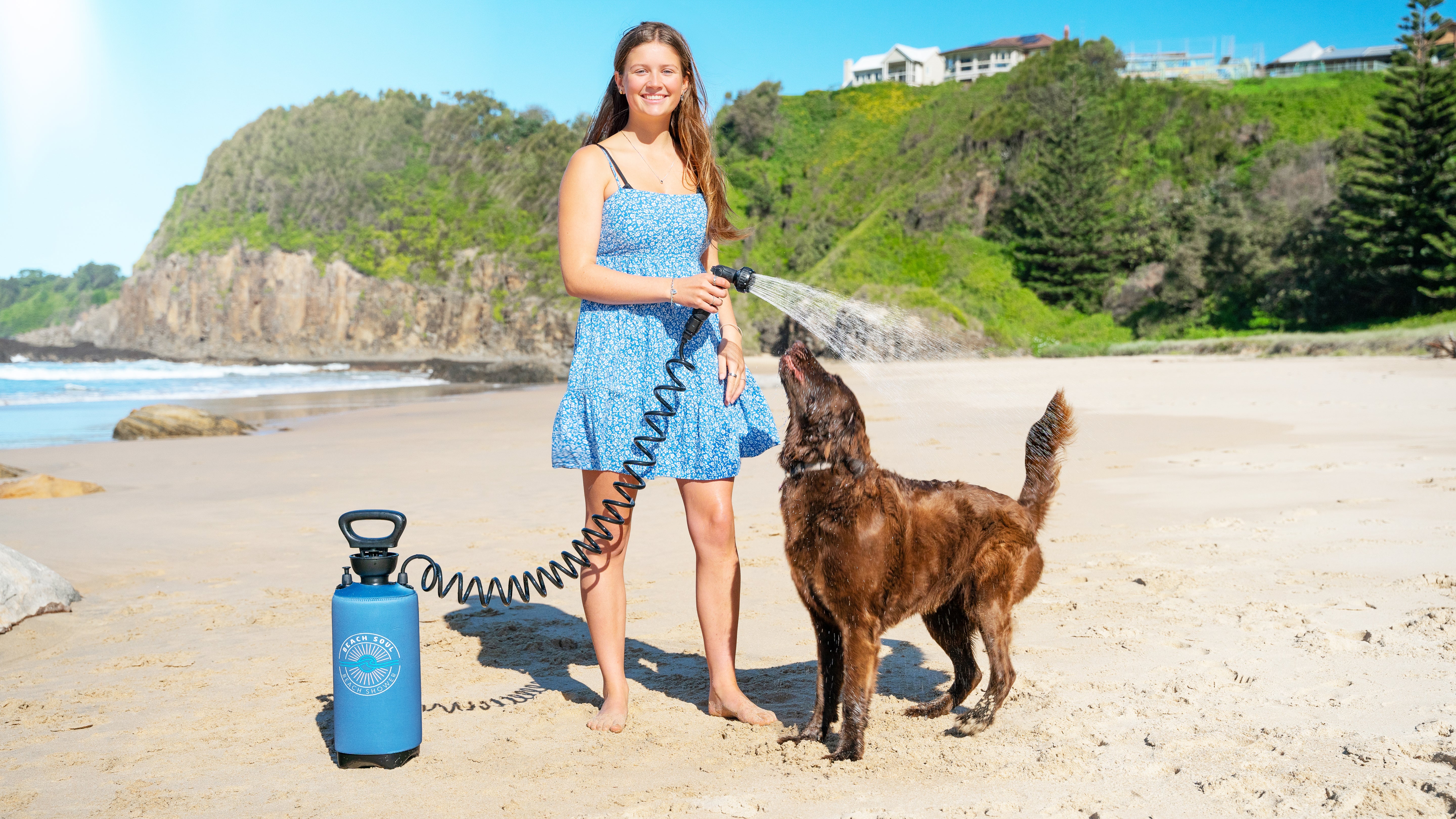 Woman using a Beach Soul portable shower to rinse a dog at the beach