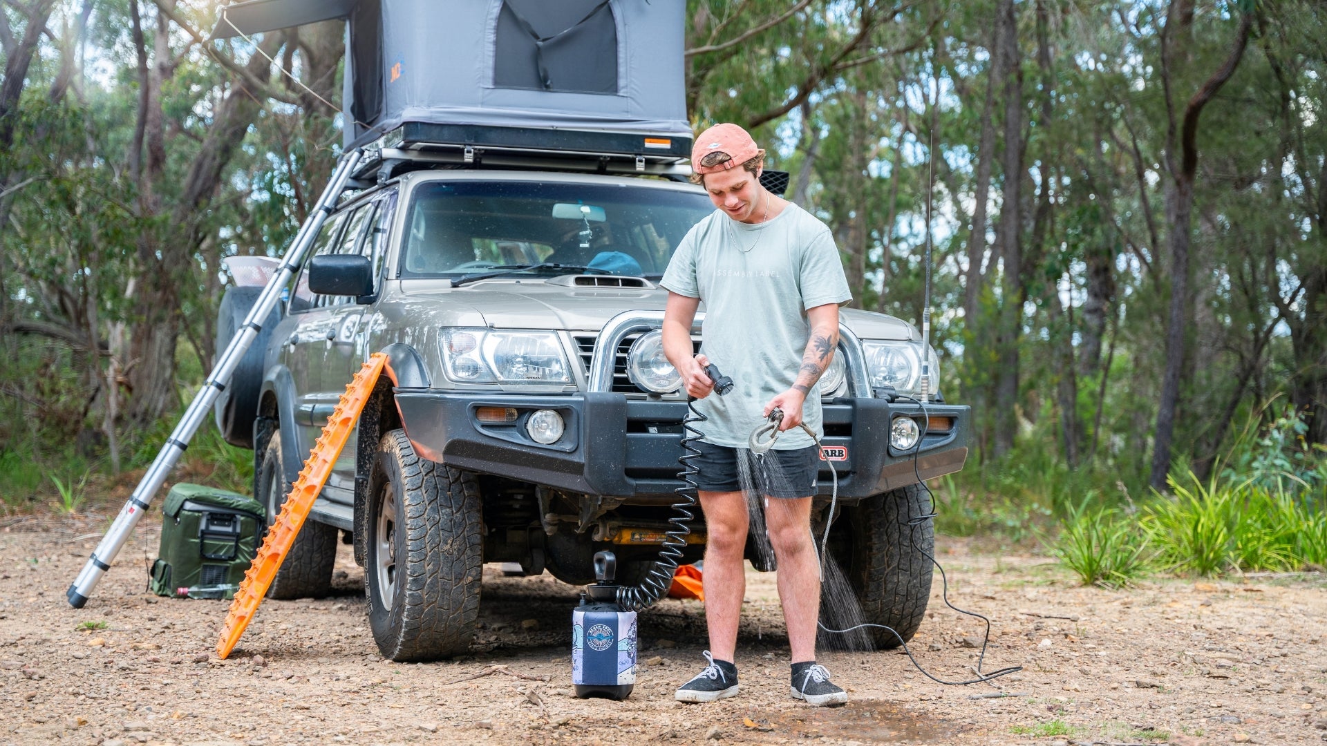 Camper rinsing off beside a four-wheel-drive with a Beach Soul portable shower