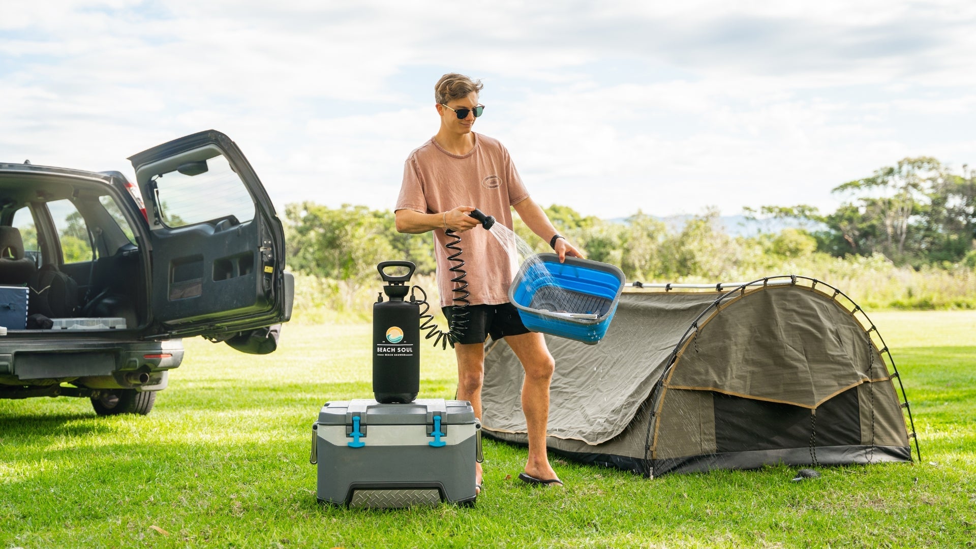 Camper using a Beach Soul manual pump portable shower beside a tent