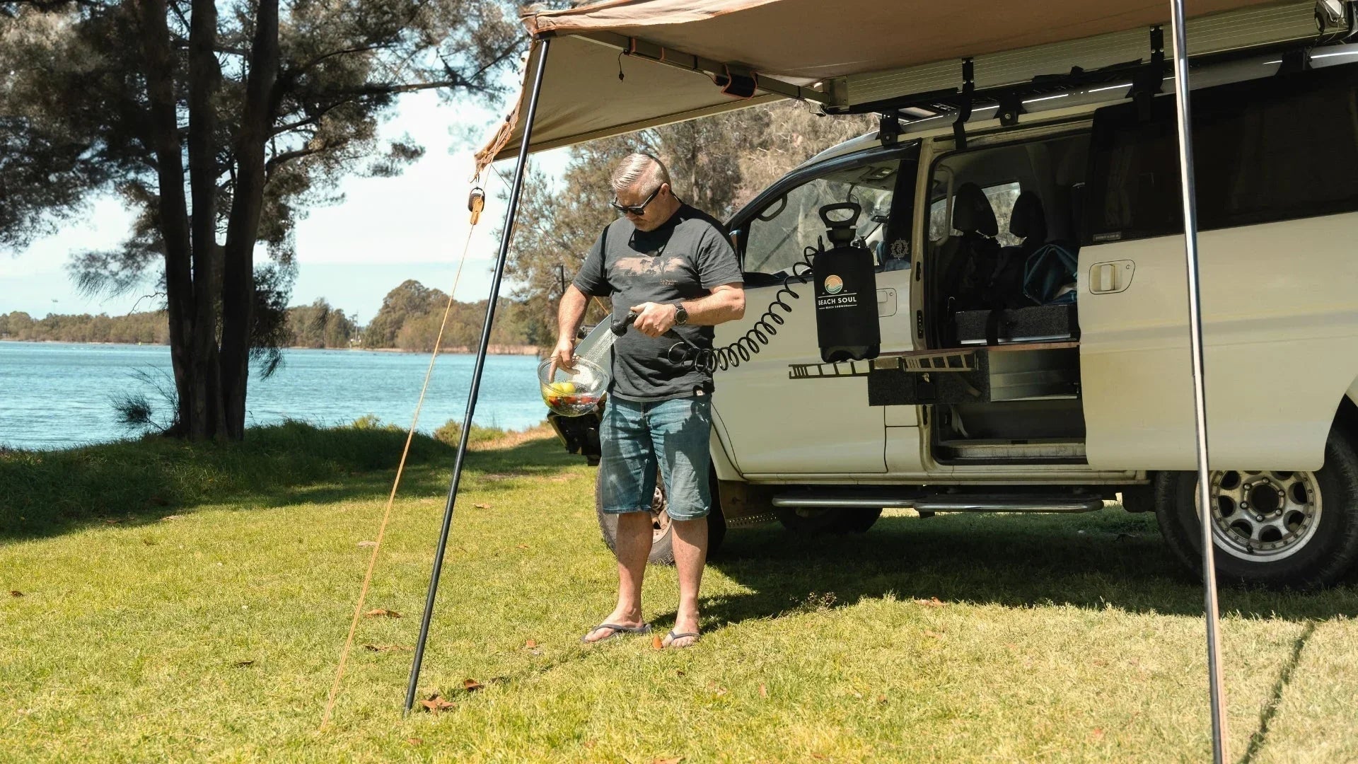Camper using a Beach Soul portable shower beside a van and campsite