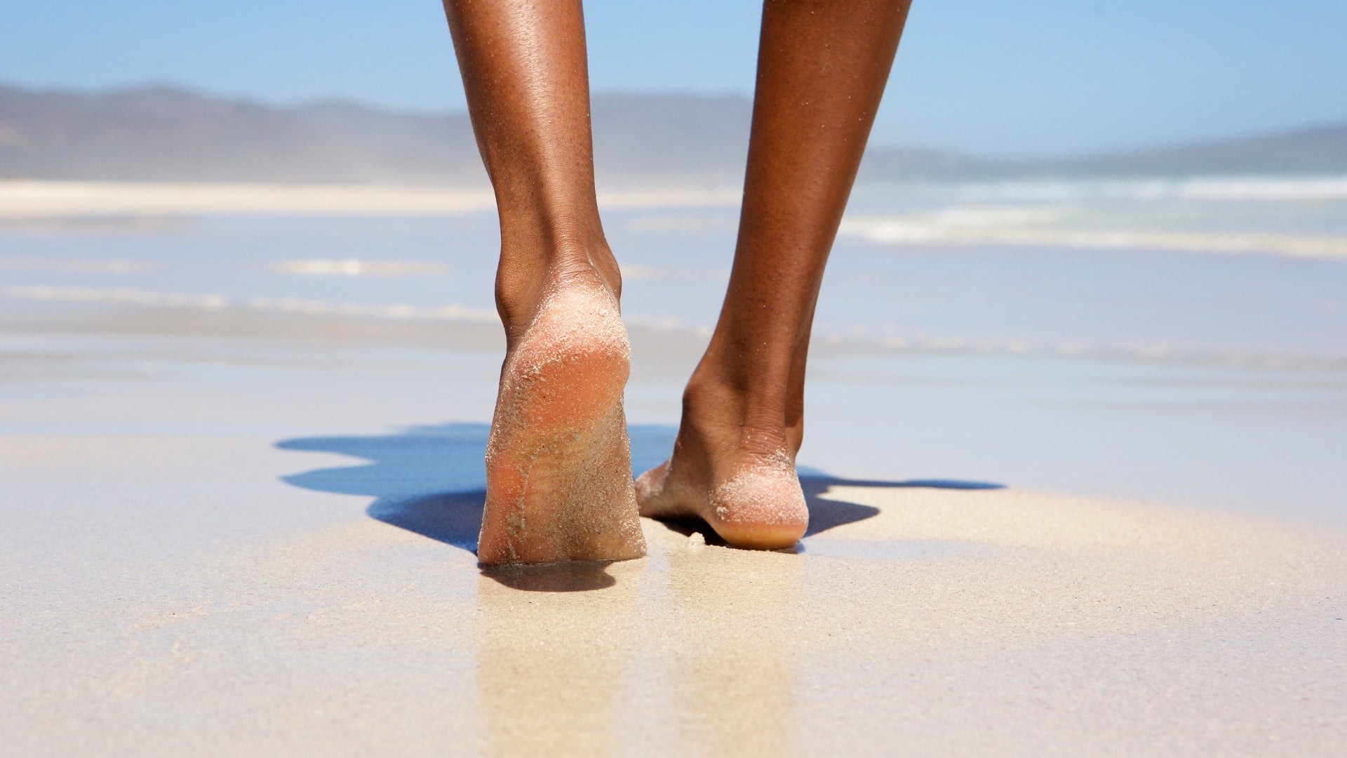 Person walking barefoot on sand beside the ocean