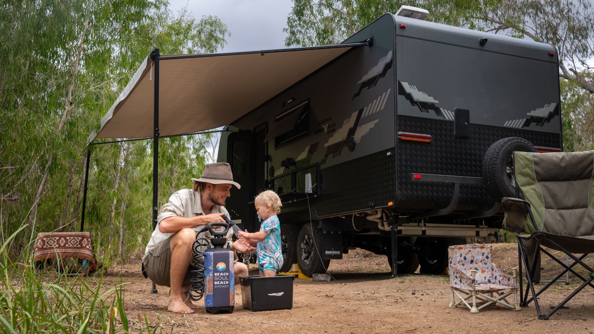 Father and child washing hands with a Beach Soul portable shower beside a caravan