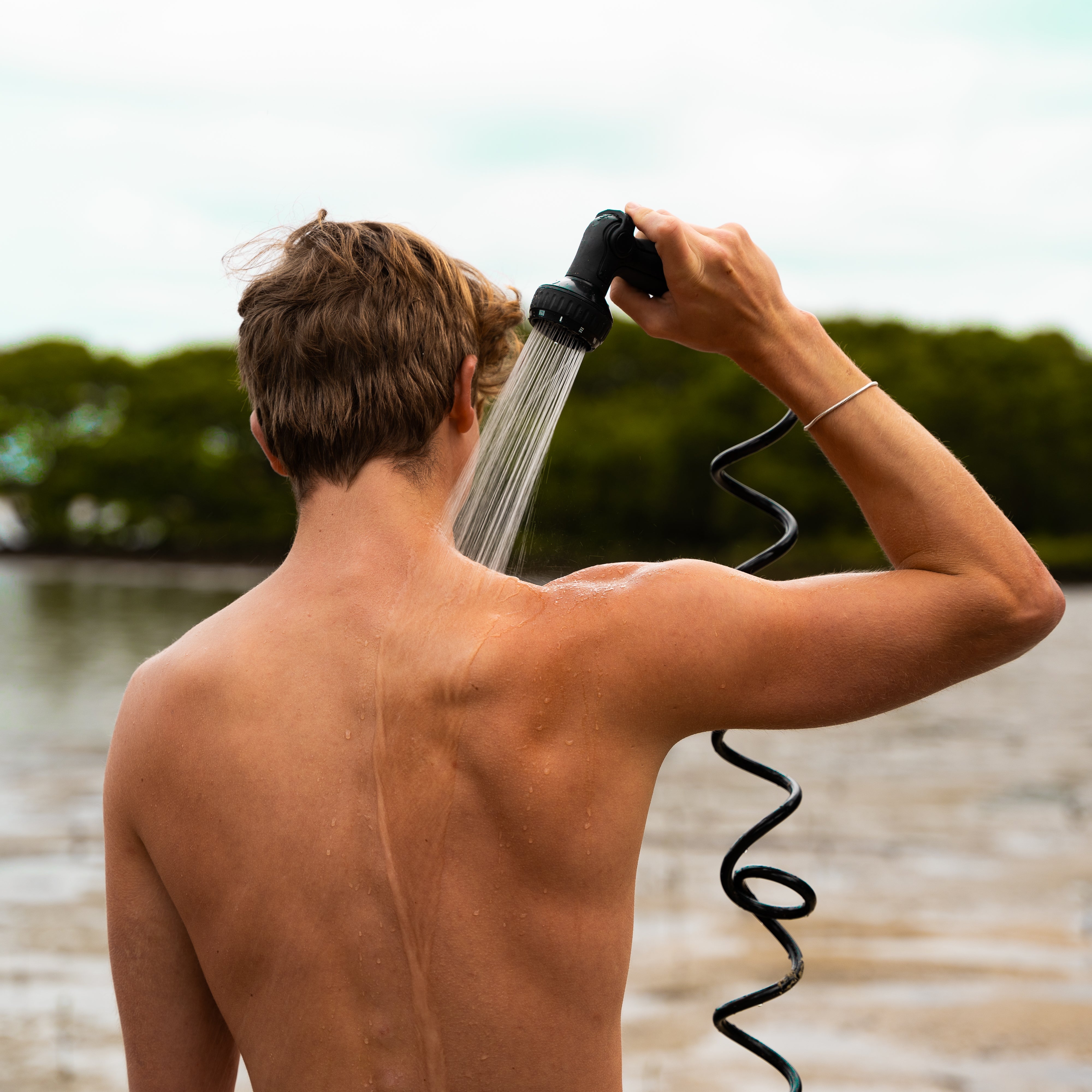Surfer rinsing with a Beach Soul portable shower after surfing