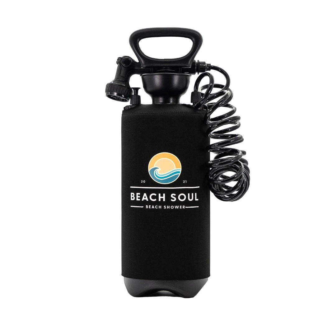 Photography of a black Beach Soul portable beach shower with a neoprene sleeve, an orange sun and blue wave logo, a coiled hose, and a top handle