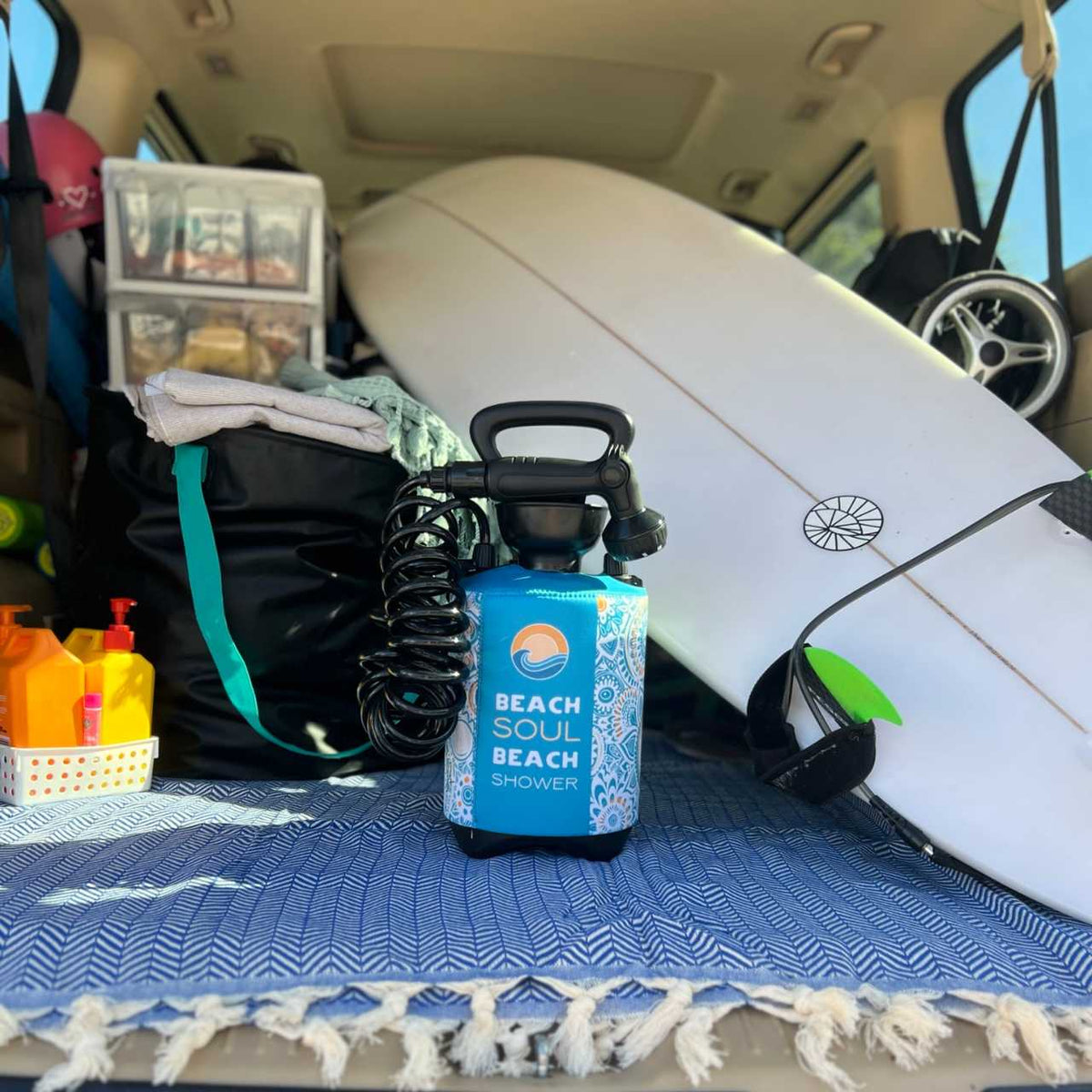 Bliss Out portable shower stored in a car with a surfboard and beach gear
