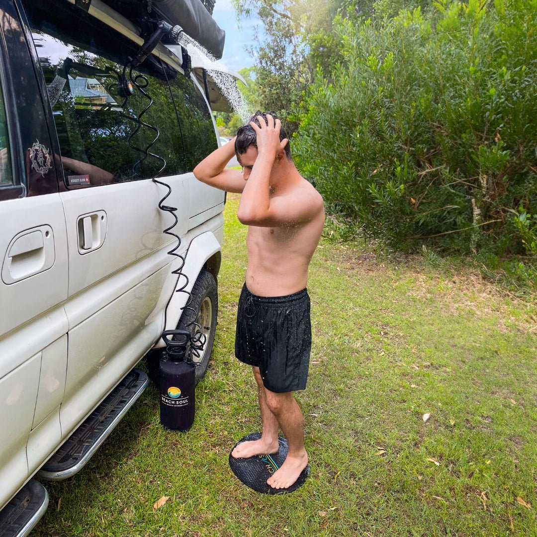 Man showering beside a van using a Beach Soul portable shower and Shower Holder