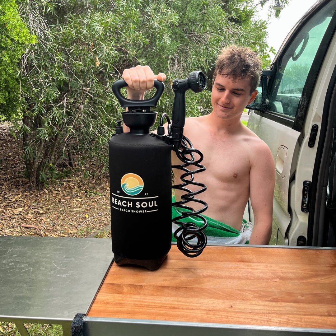 Man rinsing off beside a vehicle with a Beach Soul portable shower and Tank Clip attached
