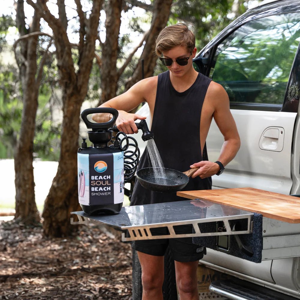 Camper using a Beach Soul portable shower to rinse cookware at a campsite