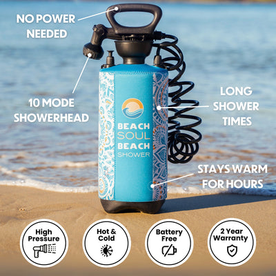 A Beach Soul portable beach shower with a vibrant blue and orange patterned insulated sleeve, black handle, and 10-mode showerhead, positioned on a sandy beach with ocean waves in the background, emphasizing its no power needed and stays warm for hours features