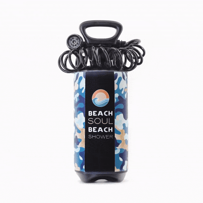 A Beach Soul portable beach shower with a blue and tan camouflage pattern, black handle, coiled hose, showerhead, and a label featuring an orange sun and blue wave logo on a white background