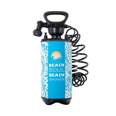 A blue and white patterned Beach Soul Beach Shower with a black top handle, adjustable spray nozzle, coiled hose, and an orange sunset wave logo on its side