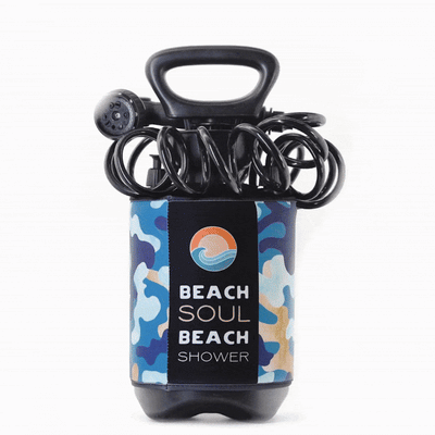 A portable Beach Soul beach shower with a black handle, coiled hose, and showerhead, wrapped in a blue and tan camouflage patterned sleeve featuring a sun and wave logo