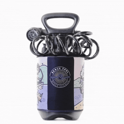 Product photo of a portable Beach Soul brand shower unit with a black handle coiled hose and multi-setting nozzle featuring a colorful neoprene sleeve with cartoon illustrations of surfers and dolphins alongside the distinct Beach Soul sun and wave logo