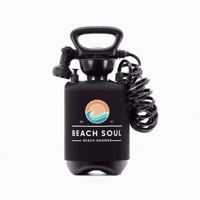 A black Beach Soul portable beach shower unit featuring an orange and teal sun and wave logo, a coiled black hose, and a shower nozzle against a white background