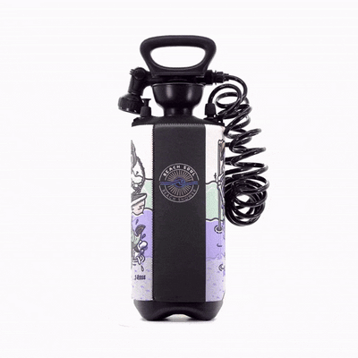 Product photo of a black portable Beach Soul Beach Shower bottle with a black handle, spray nozzle, and coiled hose, adorned with a colorful J Ross cartoon artwork sleeve featuring a skull and purple waves on a white background