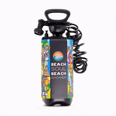Product photography of a black Beach Soul portable beach shower pump featuring vibrant artwork by T.Y. Fourestier with diverse cartoon characters and stylized beach and cityscape scenes, showcasing the prominent product logo, an ergonomic handle, and a coiled black hose
