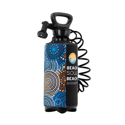 Digital photograph of a black portable beach shower bottle with a handle, coiled hose, and a vibrant aboriginal-inspired sleeve featuring blue and orange dot and swirl patterns, branded Beach Soul Beach Shower and Saltwater Dreamtime