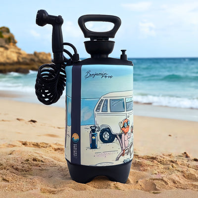 Digital illustration by Benjamin Ross adorns a light blue portable shower with a black handle and coiled hose, standing on a golden sandy beach with distant rocky cliffs and ocean waves, featuring a cartoon scene of a white VW camper van and a relaxed figure with orange hair and sunglasses in a beach chair