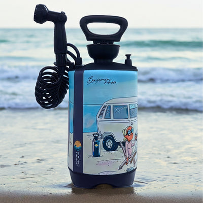 Product photography by Benjamin Ross of a portable shower product on a sandy beach featuring blue cartoon artwork with a vintage VW van and a red octopus in a beach chair by ocean waves