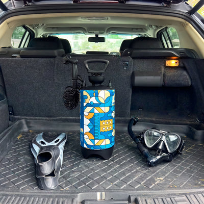 Photograph of a colorful blue, yellow, and white patterned portable shower, black and grey snorkeling fins, and a black diving mask with snorkel set arranged on a textured black mat in the trunk of a car
