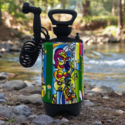 Portable NOWIE shower unit featuring a vibrant abstract art wrap depicting a woman in a bikini making a peace sign and other stylized figures, positioned on a rocky stream bank surrounded by green trees
